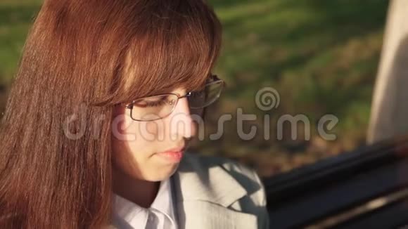 年轻的女商人戴着眼镜在公园的长椅上查看平板电脑上的电子邮件视频的预览图