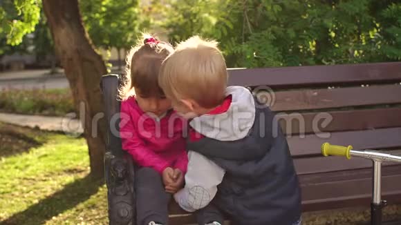小男孩在公园长椅上亲吻悲伤的小女孩视频的预览图