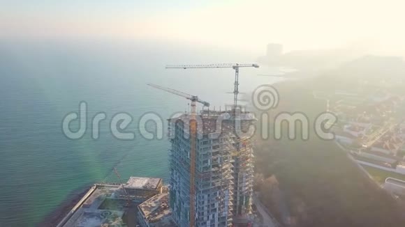空中城市景观用两台起重机在海洋上建造一座高层摩天大楼逆时针飞行光线视频的预览图