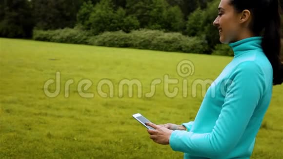 女性慢跑者站在自然小径上用手机拍一张微笑的自拍视频的预览图