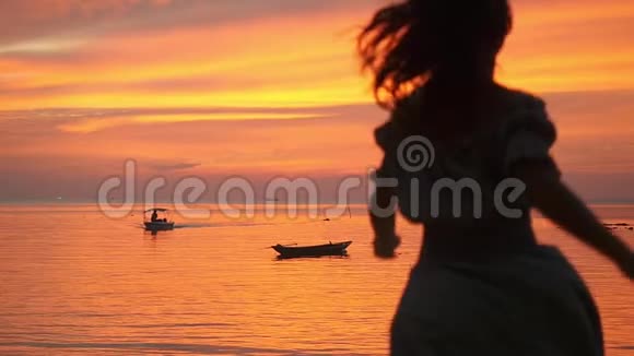 美丽的年轻女孩跑到水中在热带海滩日落的背景下旋转慢动作视频的预览图