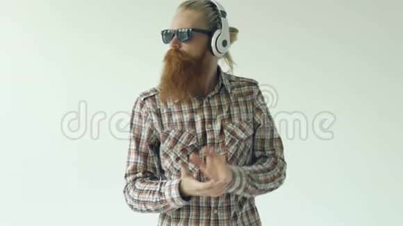 戴墨镜和耳机的快乐小胡子男人在白色背景下跳舞和听音乐视频的预览图