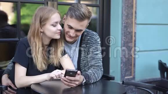 男孩和女孩坐在咖啡馆里看电话里的东西视频的预览图