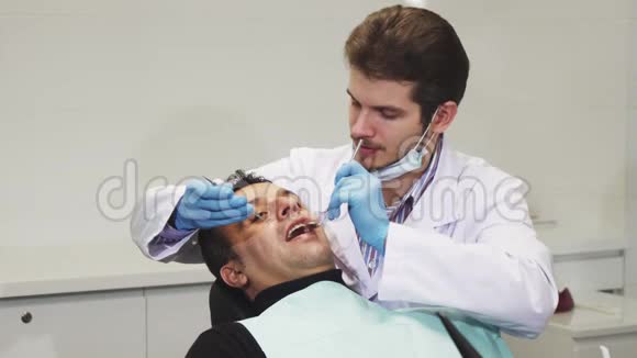 年轻的男牙科医生在检查病人时微笑视频的预览图