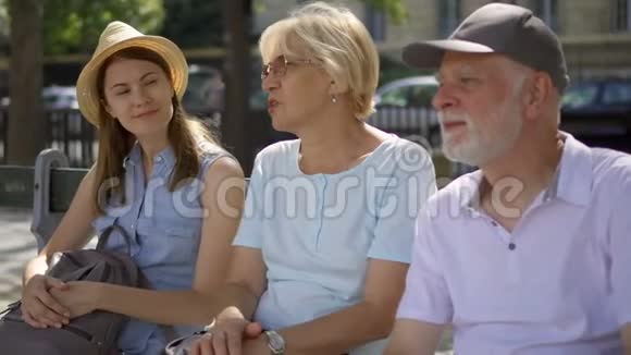 快乐的家庭享受假期老年人和他们的女儿坐在长凳上在街上放松视频的预览图