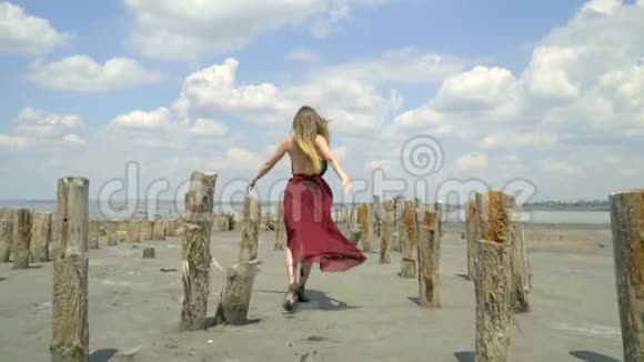 一个漂亮的金发女郎穿着一件涂在泥里的衣服在被遗弃的盐池里跳过河口回头看视频的预览图