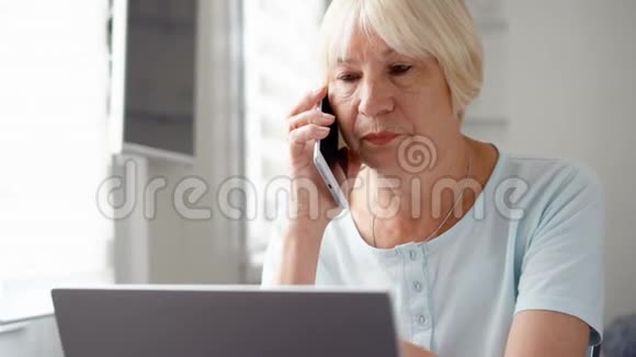 老妇人坐在家里手提电脑和智能手机通过手机在屏幕上讨论项目视频的预览图