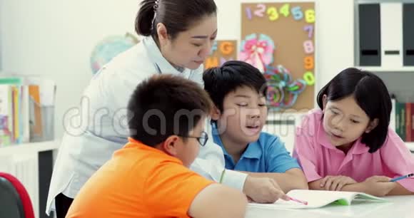 年轻的亚洲老师在课堂上帮助年幼的学生视频的预览图