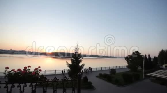 日落时美丽的湖景和海滨日落时分人们在风景如画的河堤上散步视频的预览图