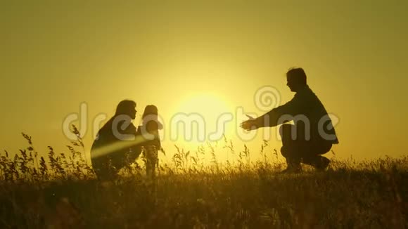 小女儿和父母在日落时跳跃在黎明的光线下爸爸妈妈和宝宝的剪影家庭概念视频的预览图