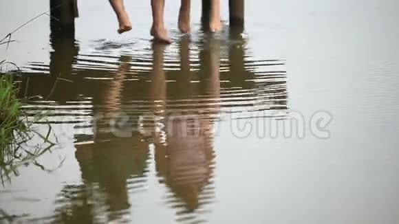 美丽的年轻夫妇坐在湖边的码头上用脚溅起水花慢动作视频的预览图