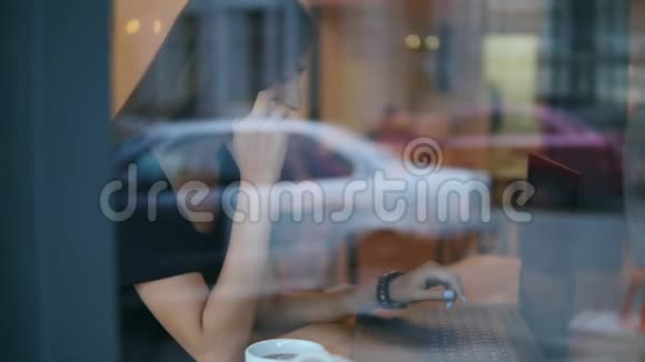 从街上看到一个迷人的年轻女人在咖啡馆里打电话看着她笔记本电脑的屏幕视频的预览图
