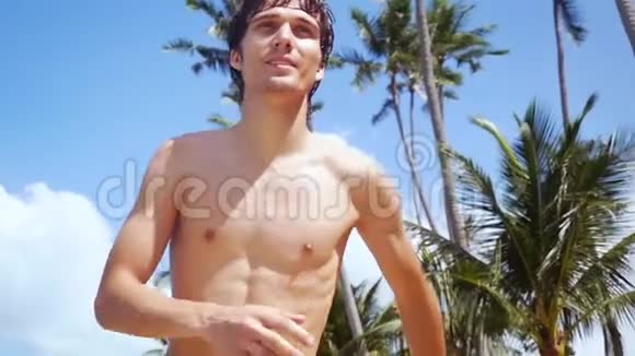 阳光明媚的一天年轻的帅哥在海滩上奔跑靠在棕榈树和背景上的蓝天上慢慢慢慢视频的预览图