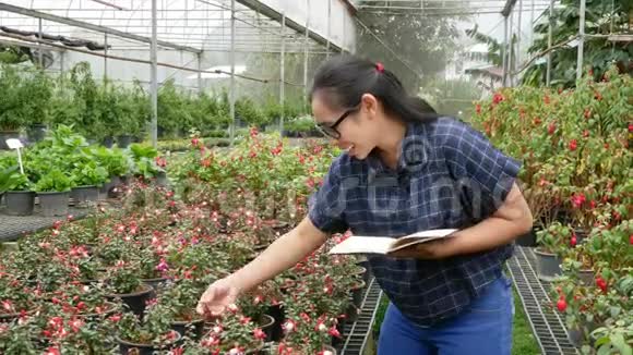 园丁亚洲妇女在温室里工作带着笔记本电脑检查农场里生长的花朵和温室里的疾病视频的预览图