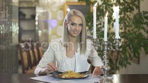 年轻的金发女郎穿着白色夹克独自一人在高档餐厅吃意大利料理意大利面做着滑稽的脸视频的预览图