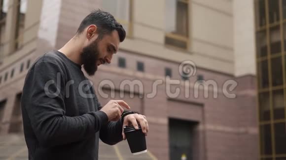 有胡子的人拿着一杯咖啡检查他的智能手表视频的预览图
