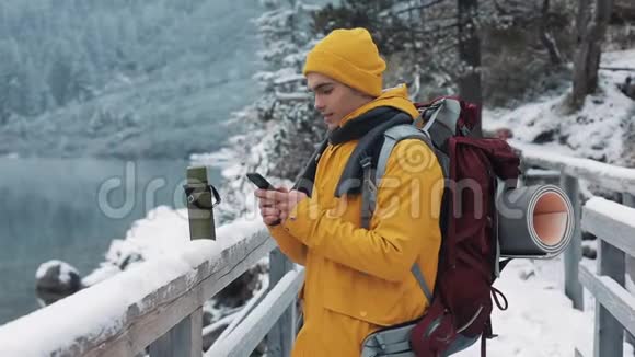 年轻的旅行者在徒步冬季旅行中使用智能手机白雪模糊的山角和湖旅行和视频的预览图