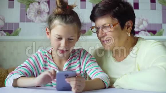 年轻可爱的孙女教祖母如何在家里使用智能手机视频的预览图