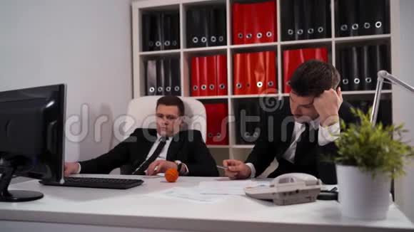 两个无聊的员工用电脑桌面在工作场所的桌子上玩小球视频的预览图