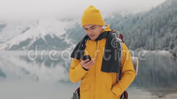 年轻的旅行者在徒步冬季旅行中使用智能手机白雪模糊的山角和湖旅行和视频的预览图