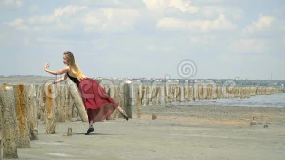一个美丽的金发女郎穿着一件连衣裙在河口中部的木柱附近跳舞站在一根绳子上视频的预览图