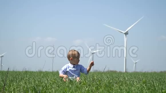 一个男孩坐在草地上在风力发电机的背景下在远处表演视频的预览图