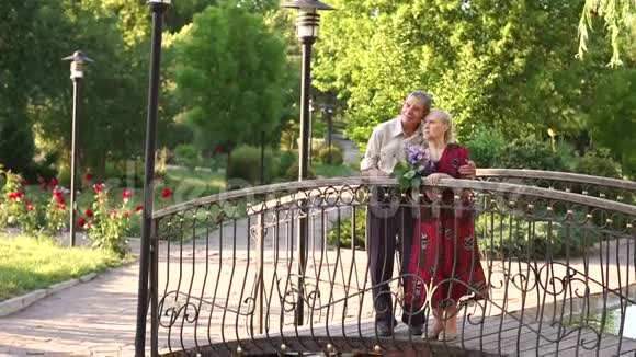 一对老年夫妇站在公园的人行桥上视频的预览图