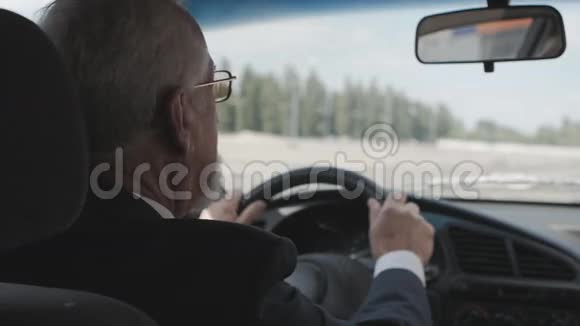 一个头发灰白夹克里有胡子的男人坐在汽车的车轮后面视频的预览图