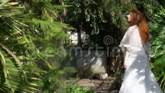 美丽的红发女孩穿着白色连衣裙在花园里旋转视频的预览图