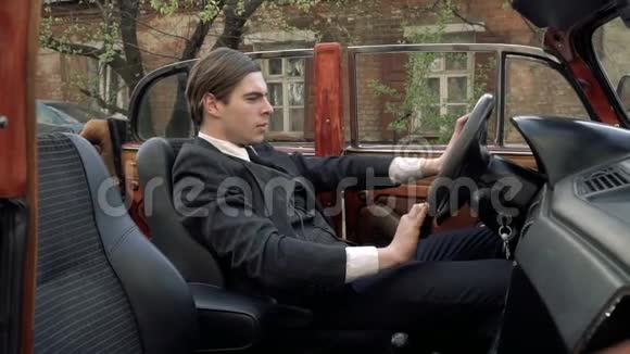 一个穿着20年代西装的男人坐在复古车的车轮前在享受着某种乐趣视频的预览图