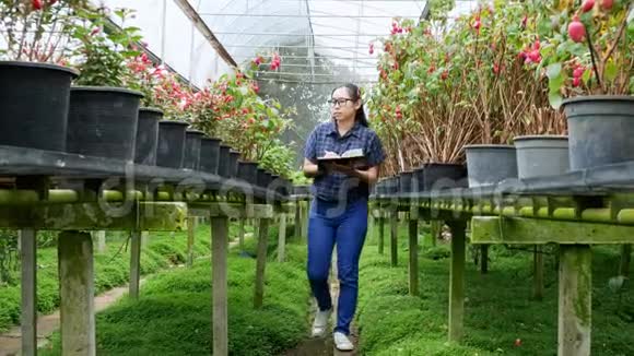 园丁亚洲妇女在温室工作带着笔记本检查农场上生长的花朵和温室里的疾病视频的预览图