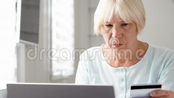 年长的女人坐在家里用笔记本电脑上的信用卡在线购物技术和老年人视频的预览图