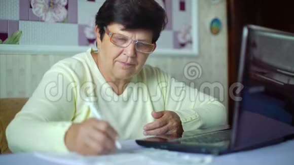 戴眼镜的老年妇女检查家里笔记本电脑的日常开支视频的预览图