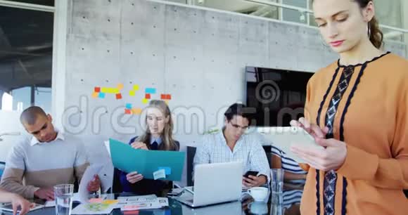 女性使用平板电脑而她的同事坐在背景4k视频的预览图