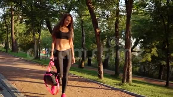 美丽的黑发女人带着运动袋在公园里散步适合健康运动的女性早晨锻炼视频的预览图