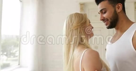 情侣拥抱微笑靠近窗户混血男人女人拥抱晨间卧室视频的预览图