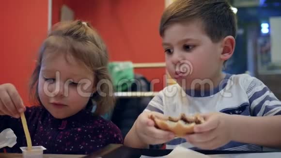 为小女孩和男孩准备的带有酱汁的法式炸薯条男孩子咀嚼汉堡包有趣的孩子在快餐中玩耍视频的预览图