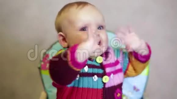 快乐的女婴坐在孩子们的椅子房间里微笑着挥舞着手臂视频的预览图