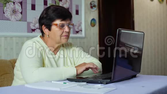 戴眼镜的老年妇女检查家里笔记本电脑的日常开支视频的预览图