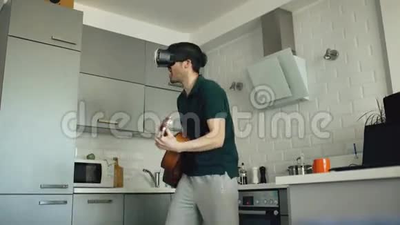 快乐的年轻人在厨房里用VR360耳机跳舞和弹吉他在家里演奏吉他视频的预览图