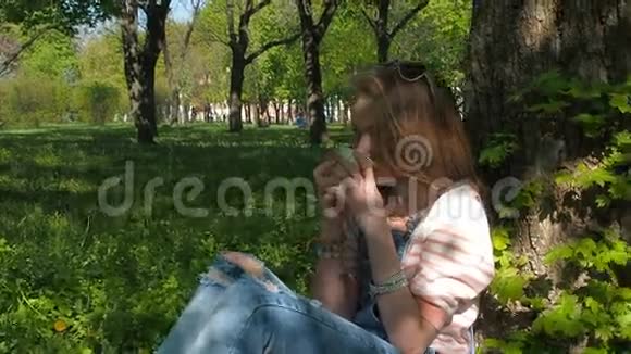 公园里的女孩喝咖啡一个十几岁的女孩穿着牛仔裤西装坐在树下那个悲伤的女孩喝咖啡视频的预览图