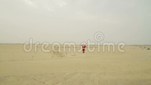 圣诞老人带着一袋礼物从沙漠来到这里圣诞老人在沙漠的沙滩上散步找到了柏油路视频的预览图