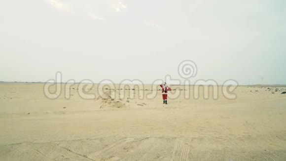 圣诞老人带着一袋礼物从沙漠来到这里圣诞老人在沙漠的沙滩上散步找到了柏油路视频的预览图
