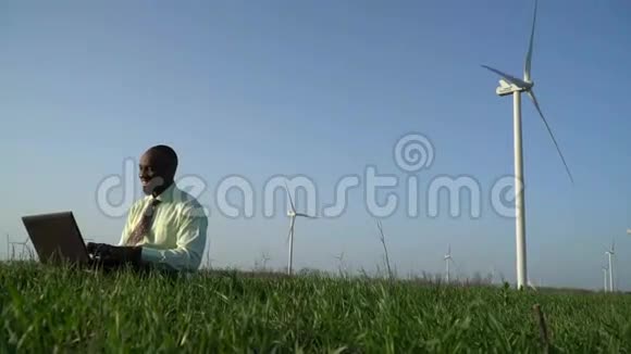 快乐的黑人坐在绿色草地上在笔记本电脑上打字视频的预览图