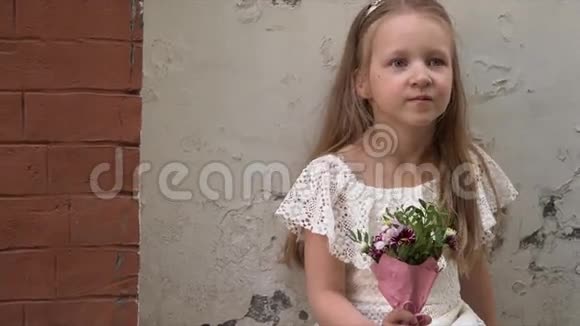 小女孩穿着一件粉红色的连衣裙和一小束漂亮的花在一堵砖墙上视频的预览图