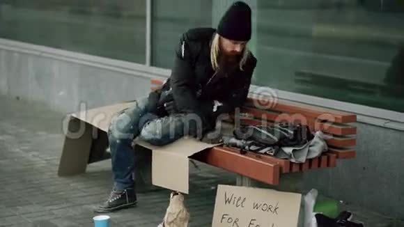无家可归的醉汉正准备在人行道上的长凳上睡觉视频的预览图