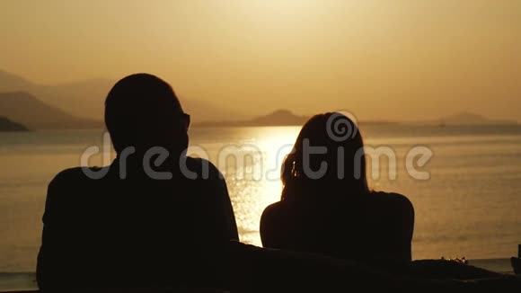 浪漫的情侣在海滩上放松在蜜月旅行假期看着令人惊叹的日落慢动作1920x1080视频的预览图