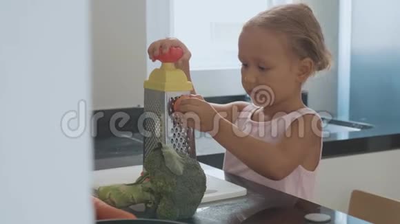 可爱的小女孩在家庭厨房的烤炉上摩擦胡萝卜视频的预览图
