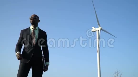 身穿商务服的黑人男士在风力发电机背景附近摘下太阳镜视频的预览图
