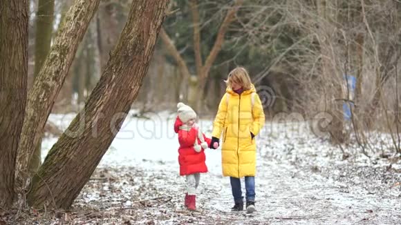年轻的母女在冬季公园散步他们穿着鲜艳的羽绒服视频的预览图